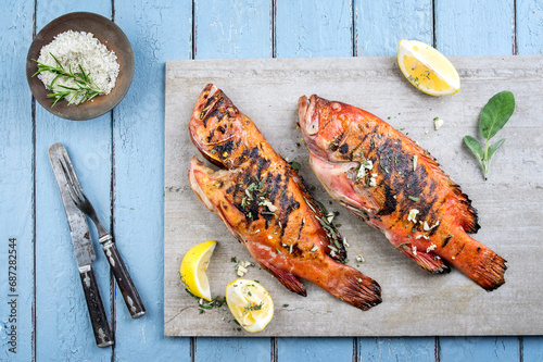 Traditional barbecue rose fish served with lemon slice, herbs and balsamico as top view on a gray design board