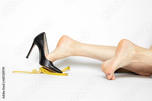 Foto Female feet in black high-heeled shoes slide on a banana peel on a white backgro