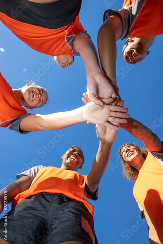Looking up at a team of female soccer players. The women are joined in unity and cheering before a match. 