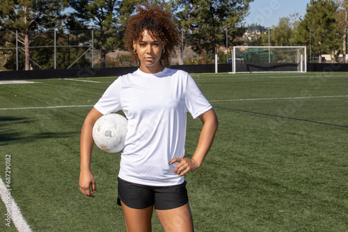 Young African American female soccer player with curly hair holding a ball on the field.  photo