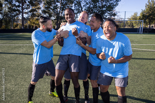 Soccer players wearing blue jerseys. The team is celebrating and the men are happy shouting and giving high fives after a score during a game. 