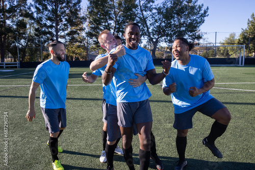 Soccer players wearing blue jerseys. The team is celebrating and the men are happy shouting and giving high fives after a score during a game.  photo