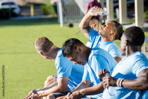 Soccer team with players sitting on the bench. They are sweaty and hot. One player is pouring water over his face and head for relief from the heat.  photo