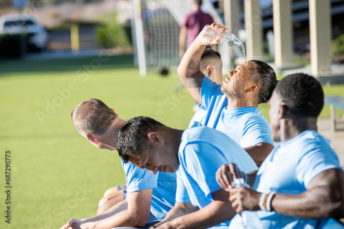 Soccer players cool off on a hot summer day outside while sitting as a team on the bench in the sun.  photo