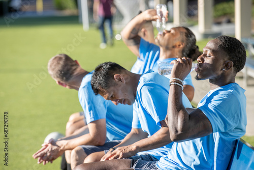 Soccer players cool off on a hot summer day outside while sitting as a team on the bench in the sun. 