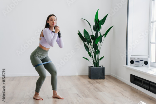 Brunette Caucasian girl in sportswear  training home with rubber expander hold hand by new artificial hand, learning to use electronic limb after injury rehabilitation.. Hi tech medicine, orthopaedics photo
