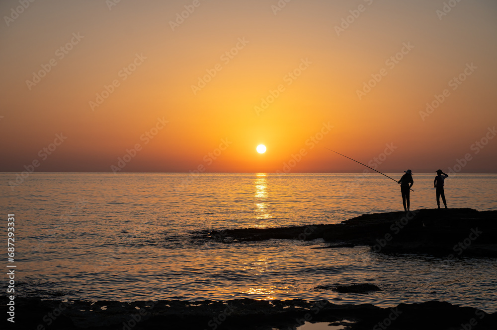 Girl and boy fishing in the sea at sunset.