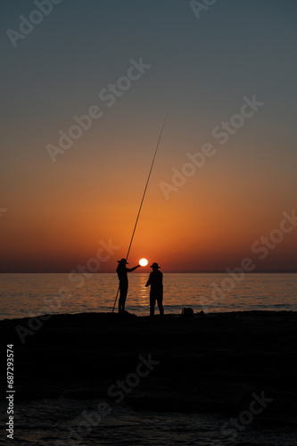 Silhouette of a girl and a man fishing with a fishing rod in the sea at sunset.