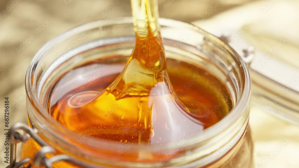 Honey dripping. Dipping honey with honey scoop in glass jar. Healthy organic food. Thick honey dripping from wooden spoon. Close-up in 4K, UHD