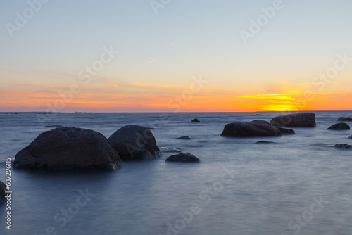 Sunset over the sea, orange strip of sunshine. Erratic boulders appearing from the water.