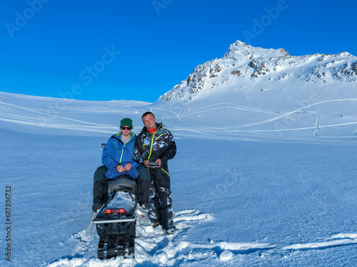 Son and father looking at drone camera while taking pictures in winter snowy mountains. Perfect sunny day, snowmobile. Sweden. Scandinavian Mountains