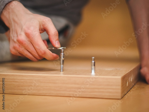 The hands of a caucasian young man with a wrench tighten a bolt on the wooden part of the bed