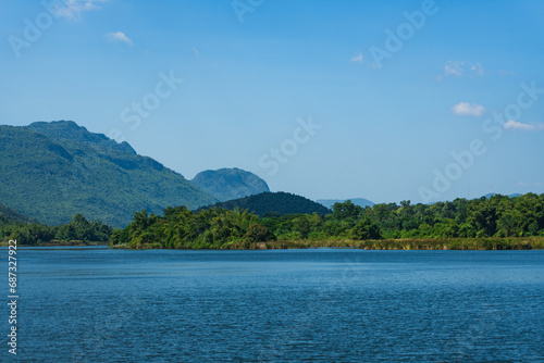 Beautiful lakeside view from a small lake in Kanchanaburi Thailand, with green trees, blue sky and sunlight
