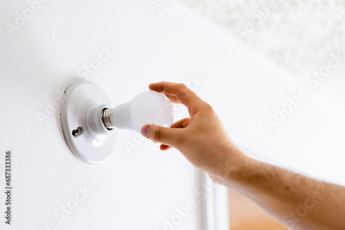 A man's hand places a light bulb on a lamp holder, white wall, housework and energy maintenance