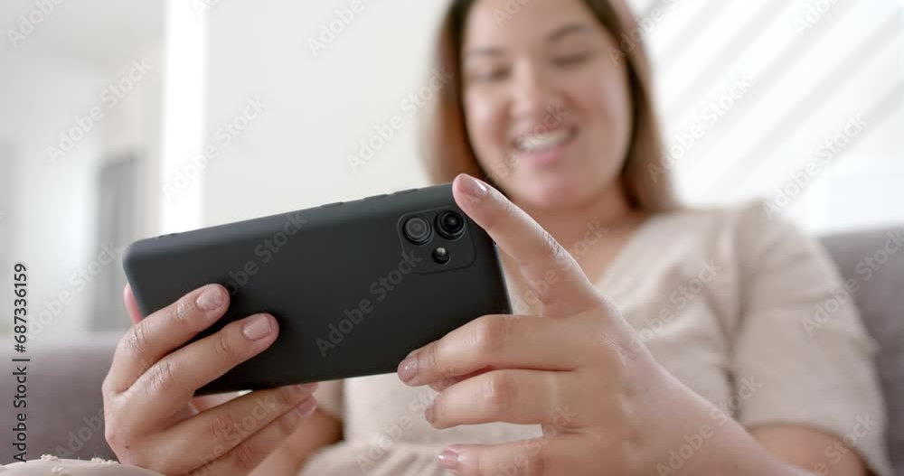 Happy plus size biracial woman having smartphone video call in sunny living room, slow motion Happy plus size biracial woman having smartphone video call in sunny living room, slow motion