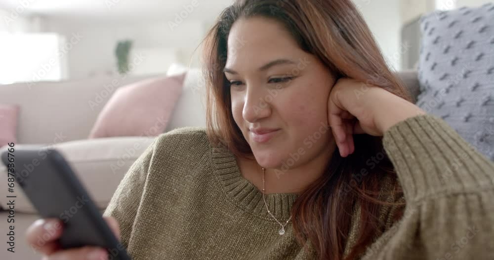 Happy plus size biracial woman relaxing in living room using smartphone, slow motion Happy plus size biracial woman relaxing in living room using smartphone, slow motion