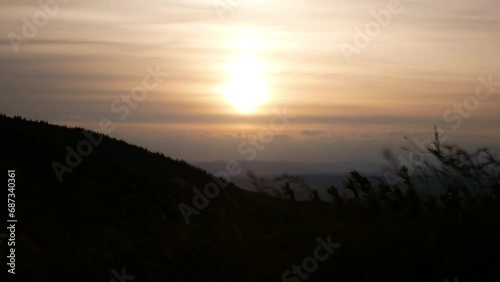 Video recording of a sunset through a dense layer of clouds in the mountains. The spikelets and the mountain in the foreground became black as shadows.