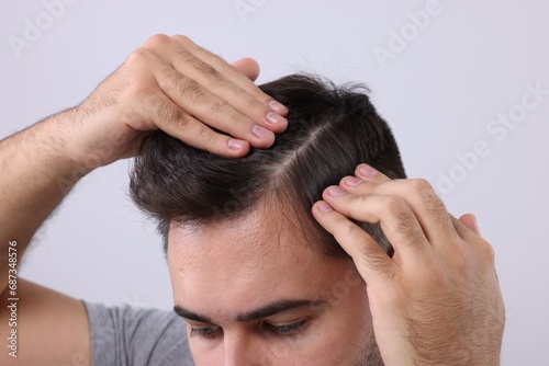 Man examining his head on light grey background, closeup. Dandruff problem
