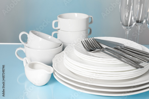 Set of clean dishes, glasses and cutlery on light blue table, closeup