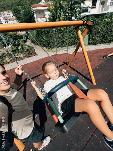 Dad swings a little girl on a chain swing at the playground