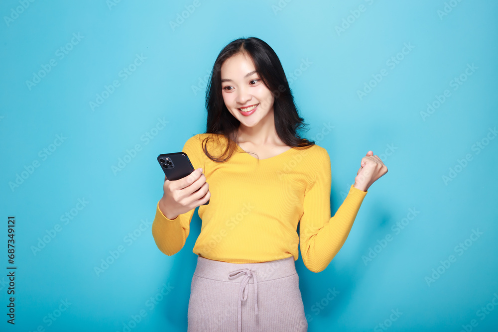 A beautiful woman poses very cheerfully and happily while holding a cell phone in her other hand, light blue background. A beautiful woman poses very cheerfully and happily while holding a cell phone in her other hand, light blue background.