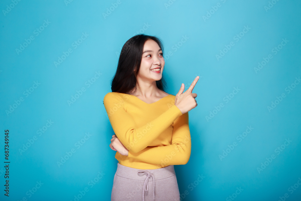 Standing and pointing happily, Portrait of a friendly young woman smiling happily, Beautiful girl on the light blue background showing point fingers poses.
