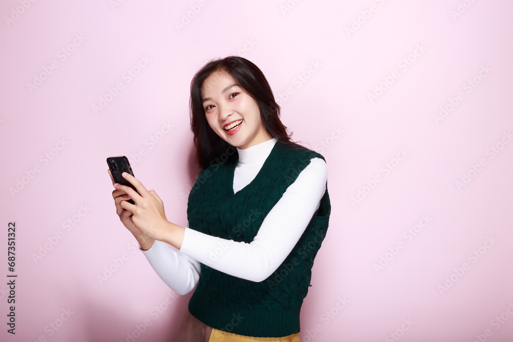 A woman has a pink background as a backdrop for a single portrait, smiling and holding a cell phone in her hand, pink background. A woman has a pink background as a backdrop for a single portrait, smiling and holding a cell phone in her hand, pink background.