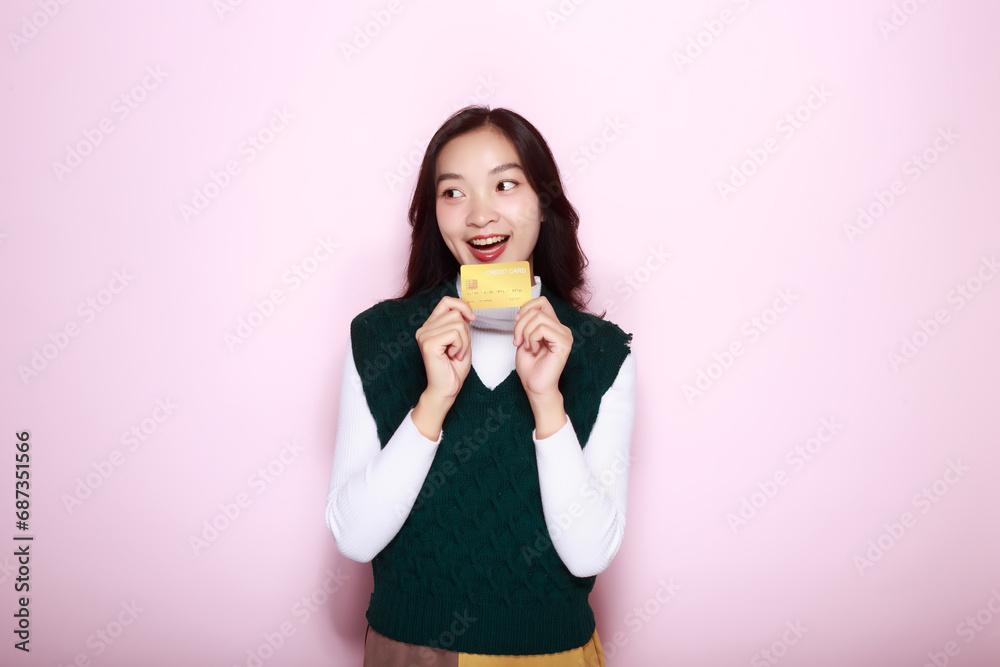 Asian woman posing with a credit card while standing in front of a light pink background.