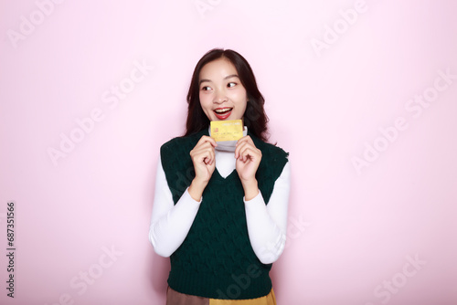 Asian woman posing with a credit card while standing in front of a light pink background.