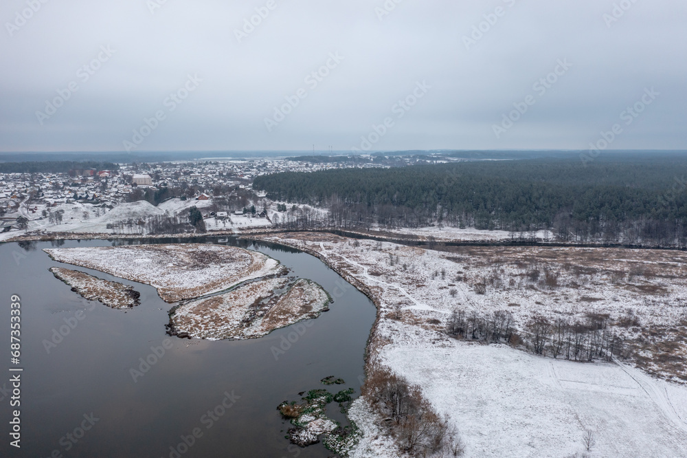 Beautiful winter aerial landscape. A river and a lake forming islets along the coast, with a river bridge, forest and a small town on the horizon.