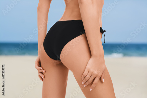 Woman in stylish bikini on sandy beach near sea, closeup