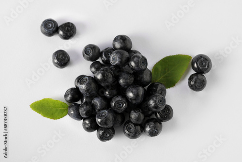 Pile of ripe bilberries and leaves on white background, flat lay