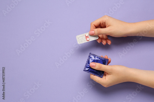 Woman holding condom and contraceptive pills on violet background, top view with space for text. Choosing birth control method photo