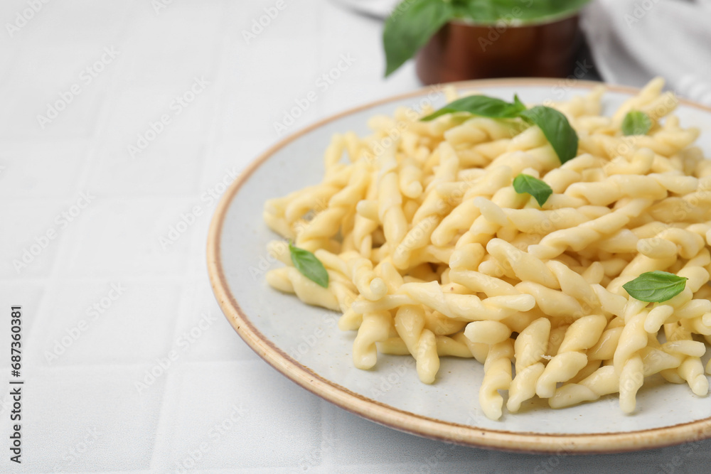 Plate of delicious trofie pasta with basil leaves on white tiled table, closeup. Space for text Plate of delicious trofie pasta with basil leaves on white tiled table, closeup. Space for text