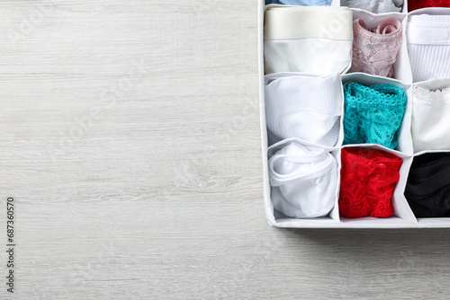 Organizer with folded women's underwear on light wooden table, top view. Space for text photo