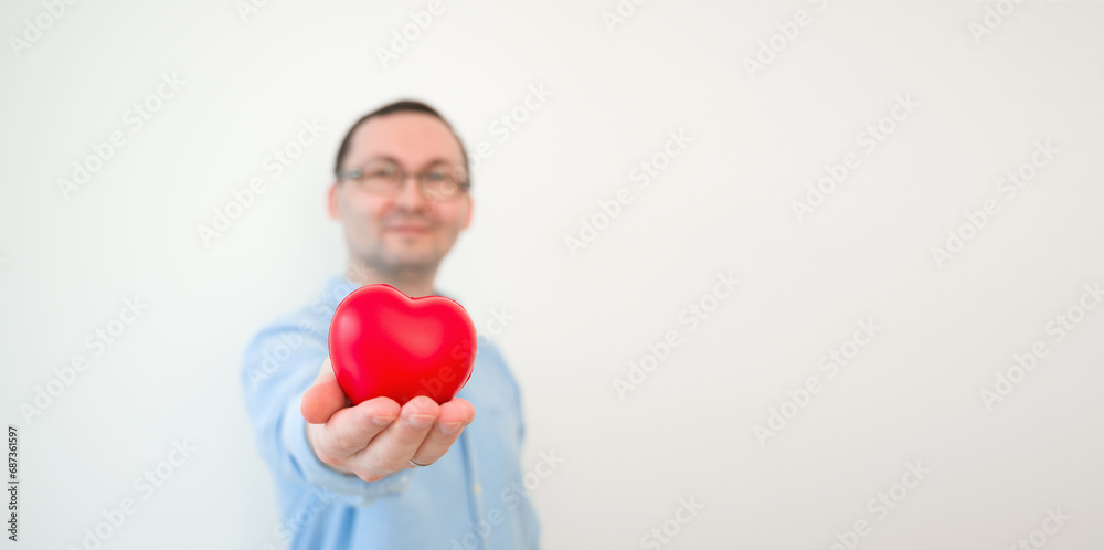 Young smiling man holding heart against white wall. VAlentines banner with place for text Young smiling man holding heart against white wall. VAlentines banner with place for text