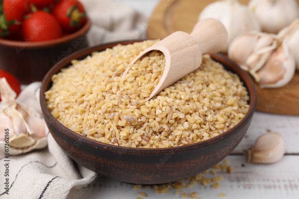 Bowl and scoop with raw bulgur on white wooden table, closeup Bowl and scoop with raw bulgur on white wooden table, closeup