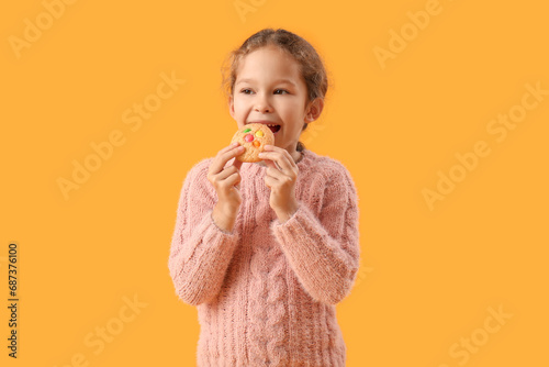 Cute little girl eating tasty cookie on yellow background