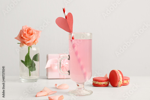 Glass of tasty cocktail with cakes and rose on wooden table against white background. Valentine's Day celebration