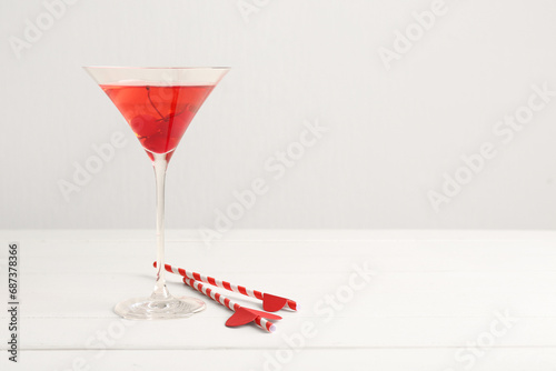 Glass of tasty cocktail with straws on wooden table against white background. Valentine's Day celebration