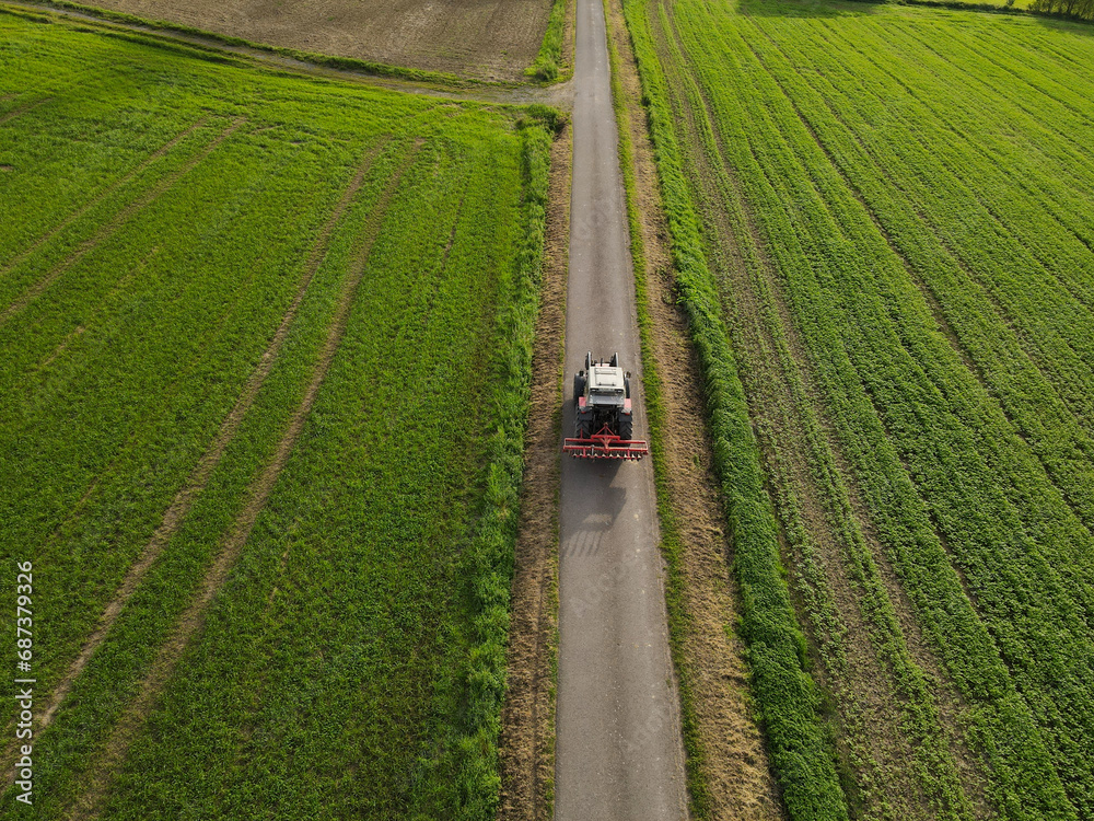 Driving tractor between fields on an asphalt path in the countryside from above  