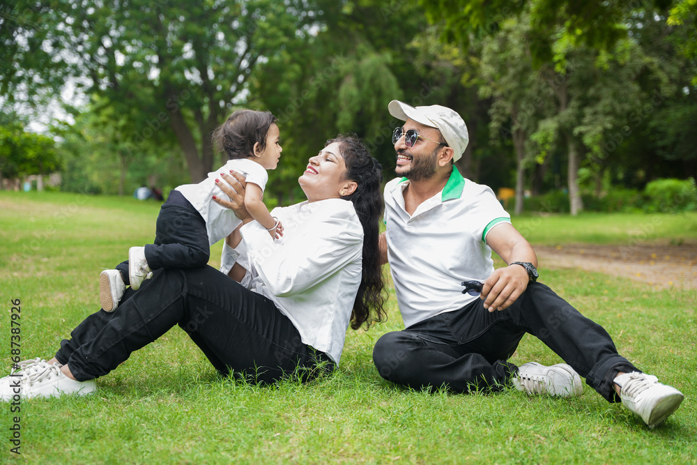 Happy Young indian parents with their cute little adorable daughter playing in park or garden. lifestyle concept.