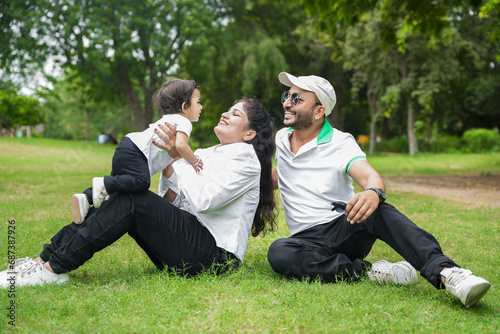 Happy Young indian parents with their cute little adorable daughter playing in park or garden. lifestyle concept.