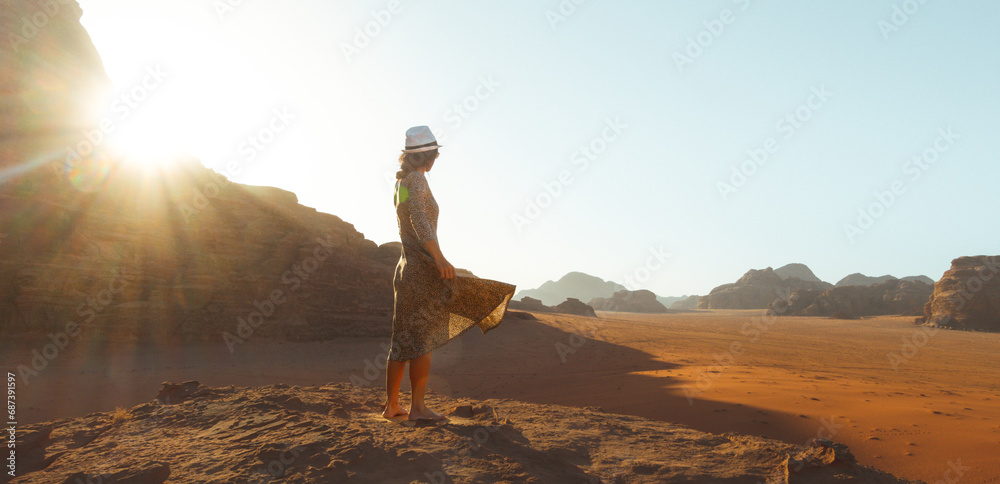 Close up woman tourist in dress stand on cliff barefoot at viewpoint enjoy sunrise on holiday vacation in beautiful Wadi rum desert, Jordan. Popular travel destination middle east - obrazy, fototapety, plakaty 