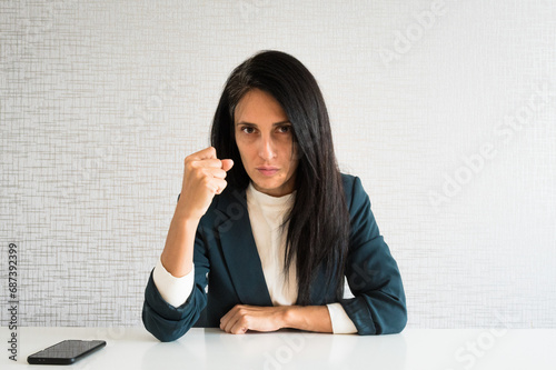 Young cute caucasian brunette business woman director in office show fist to camera at work for employee resentful angry serious look at camera. POV employee photo