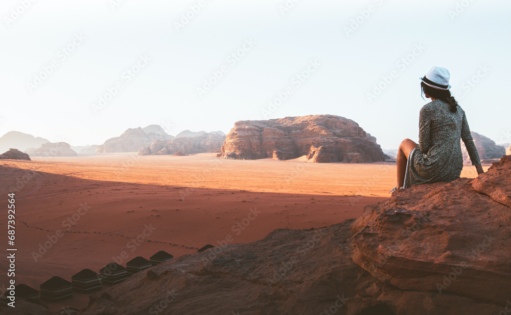 Woman tourist in dress sit on cliff at viewpoint on sunset in Wadi Rum desert - valley Wadi Saabit. Jordan explore concept