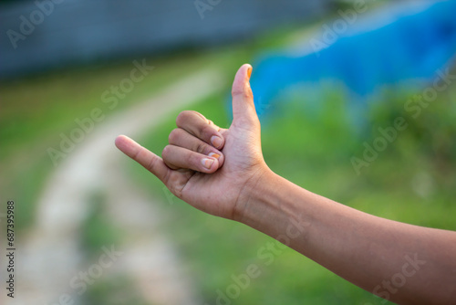 A man has his thumb pointing up one finger forward and blurred background © Rokonuzzamnan