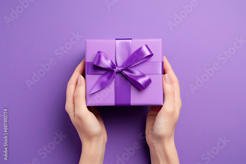 top view hand holding a purple gift box with ribbon on a violet background © Rangga Bimantara