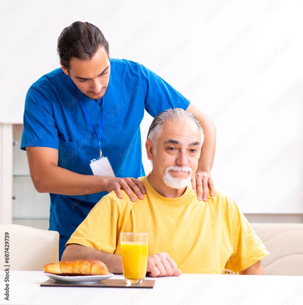 Young male doctor visiting old patient at home