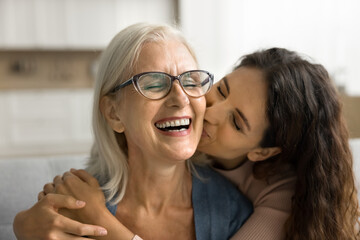 Happy loving adult daughter kissing cheerful laughing mature mum with love, gratitude, congratulating on mothers day, enjoying family meeting, visit, friendship, leisure time